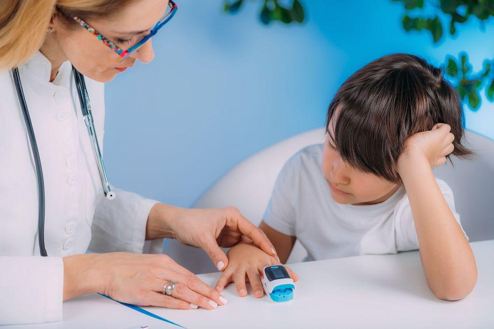 Pediatra controlando el nivel de oxígeno en sangre de un niño con un oxímetro